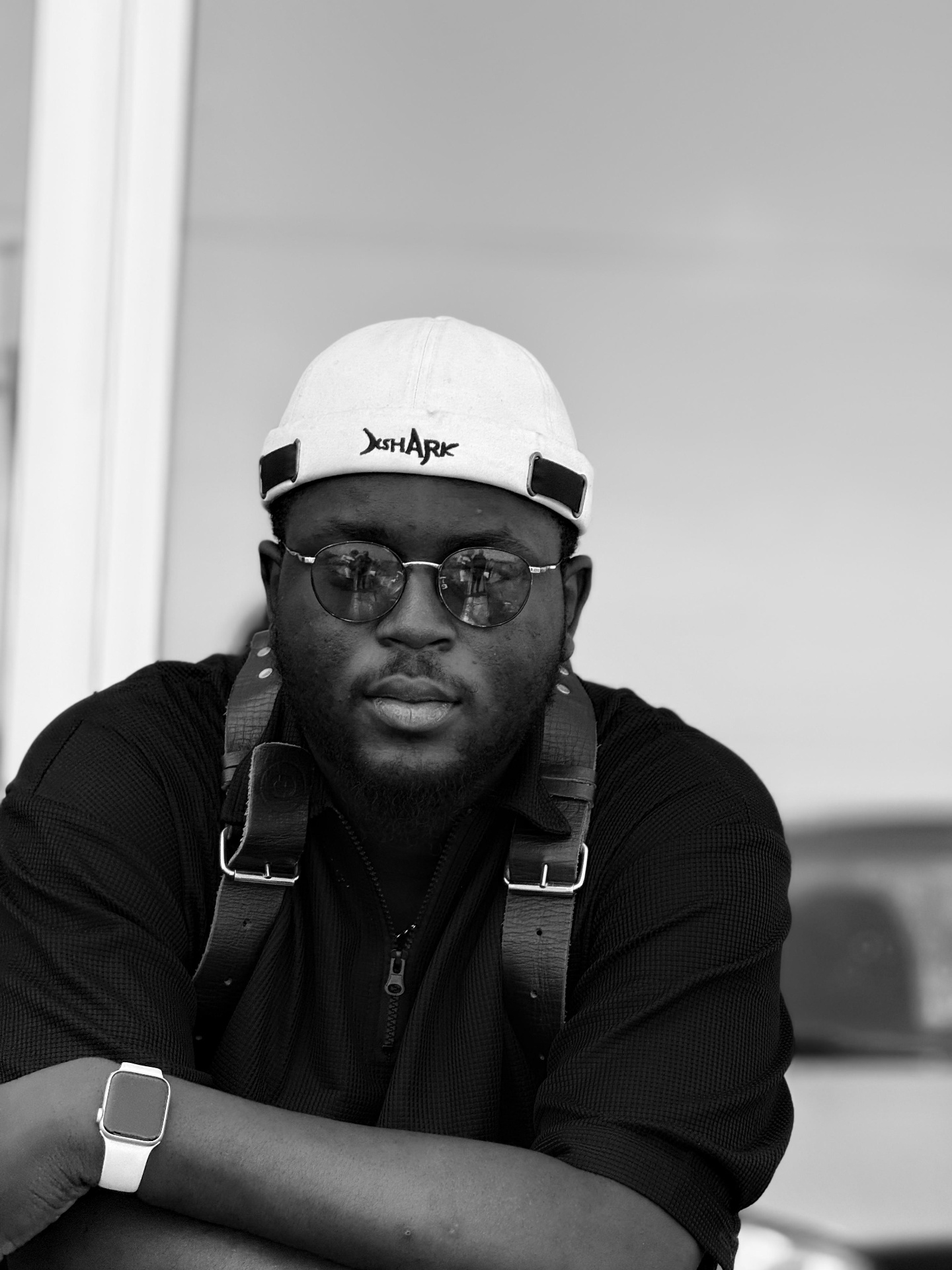 Black and white portrait of Oche with camera strap and cap
